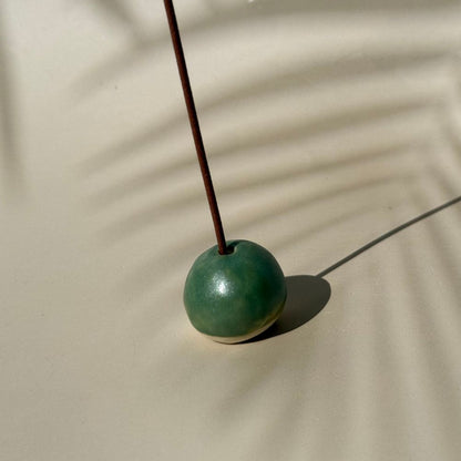 Green incense holder with a single incense stick on a beige surface