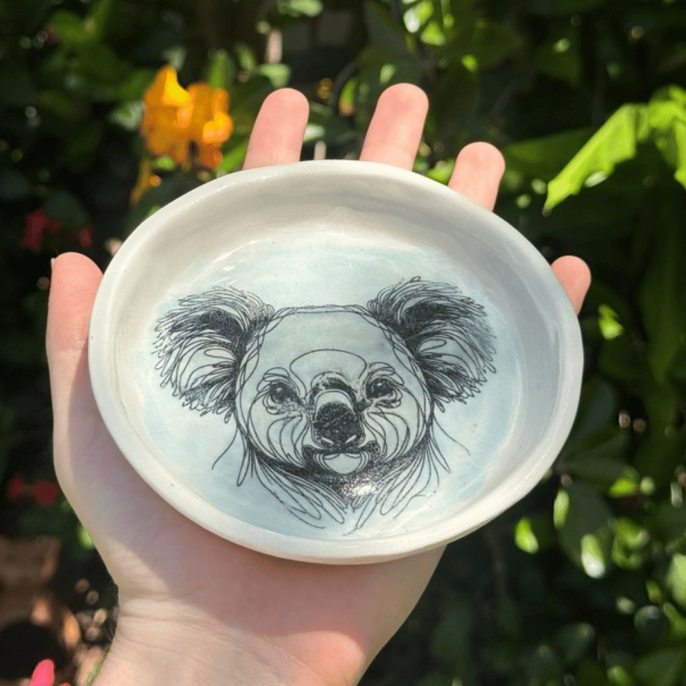 Hand holding a ceramic plate with a koala design against a natural background