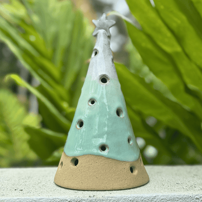 Ceramic incense burner shaped like a Christmas tree with a star on top, set against a green leafy background. Handmade in Australia.