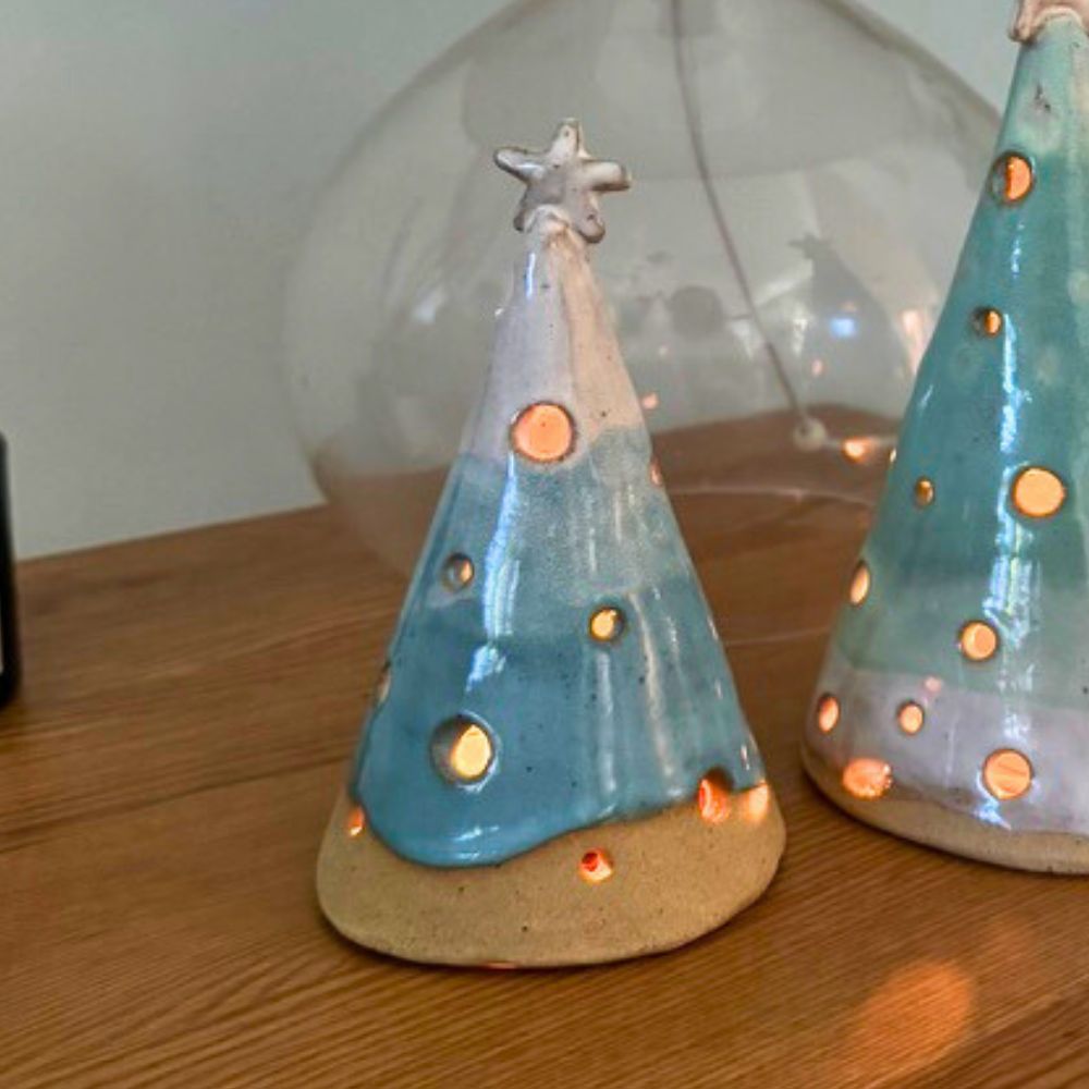 Two blue ceramic Christmas trees with star on a wooden surface.
