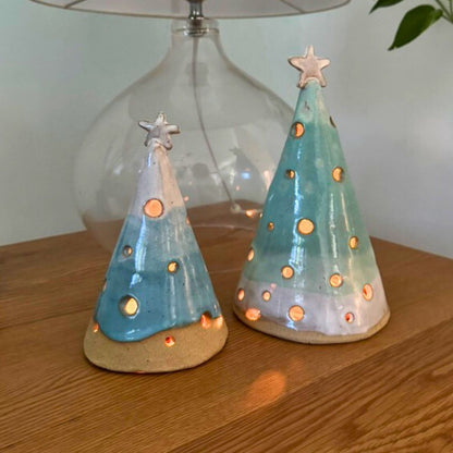 Two ceramic Christmas tree luminary cones on a wooden surface with a neutral background.