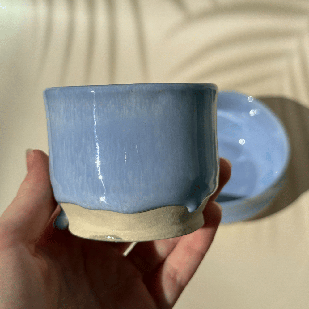 Hand holding a lilac ceramic cup with a plain background