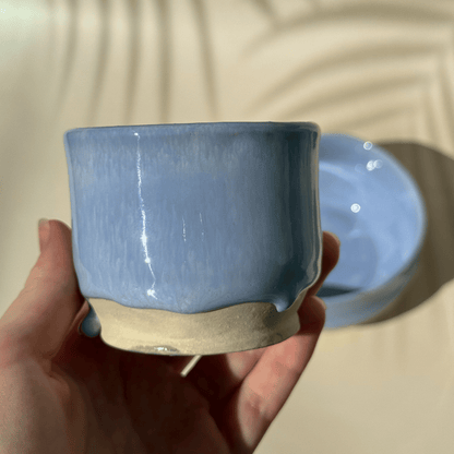 Hand holding a lilac ceramic cup with a plain background