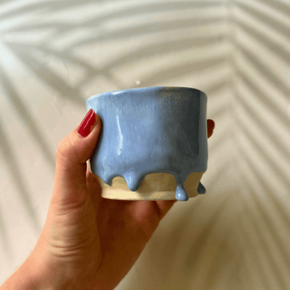 Hand holding a small lilac ceramic pot against a neutral background