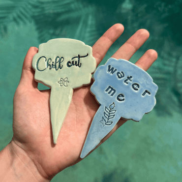 Two plant markers with 'Chill out' and 'Water me' text held against a green background. Sunshine PotTree.