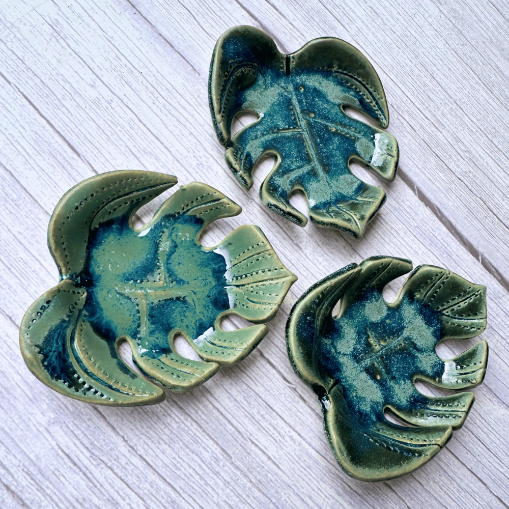 Three ceramic leaf-shaped dishes with a green and blue glaze on a light wooden surface.