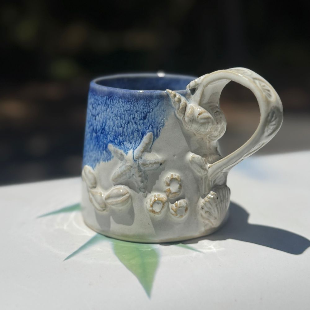 Ceramic mug with decorative handle and blue glaze on a white surface