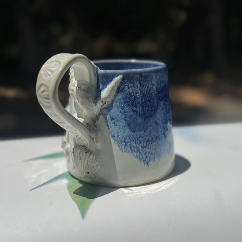 Ceramic mug with swan handle on a reflective surface