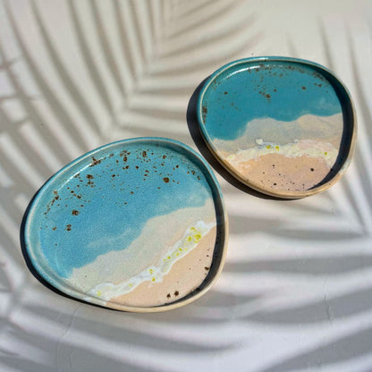 Two ceramic plates with a beachscape design on a white surface.