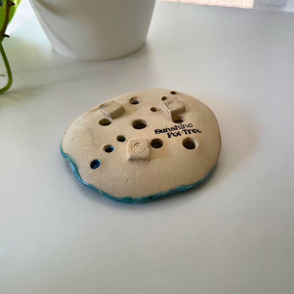 Round ceramic product with holes and 'Sunshine Pottery' text on a white surface