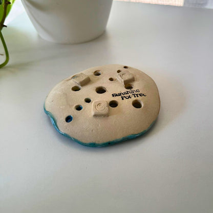 Round ceramic product with holes and 'Sunshine Pottery' text on a white surface