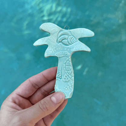 Hand holding a light blue ceramic Palm Tree decorative item against a teal background. Sunshine Pot-Tree, Sunshine Coast, Queensland, Australia