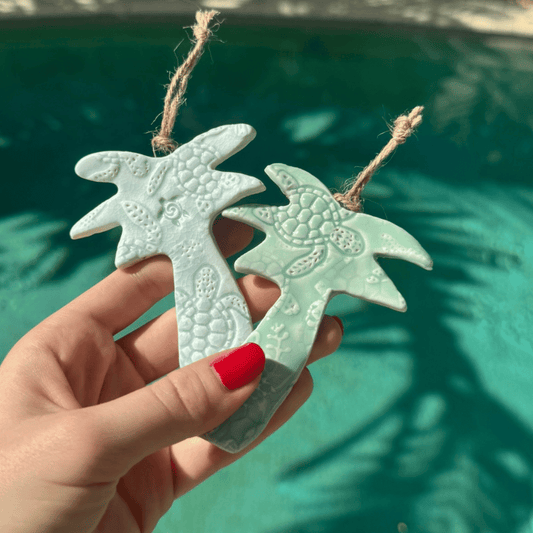 Hand holding two palm tree shaped ceramic ornaments against a blurred green background. Sunshine Pot-Tree, Sunshine Coast, Queensland, Australia