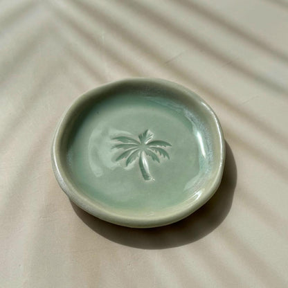 Green ceramic dish with a palm tree design on a beige surface