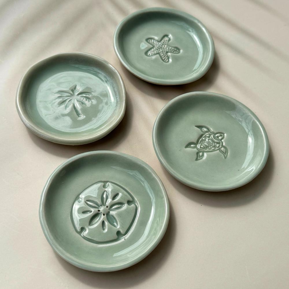 Four green ceramic plates with embossed designs on a beige surface