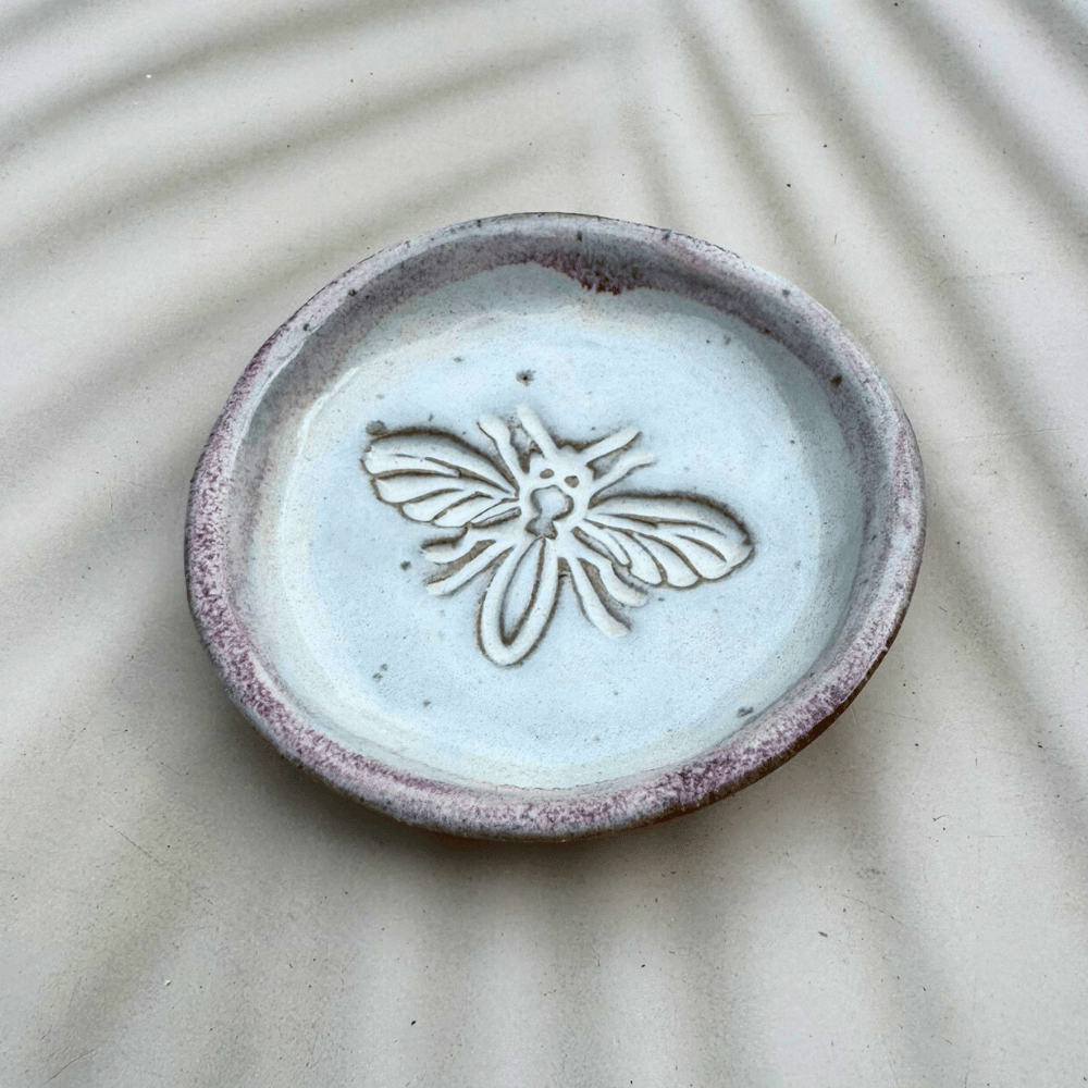 Ceramic dish with bee design on a textured beige background