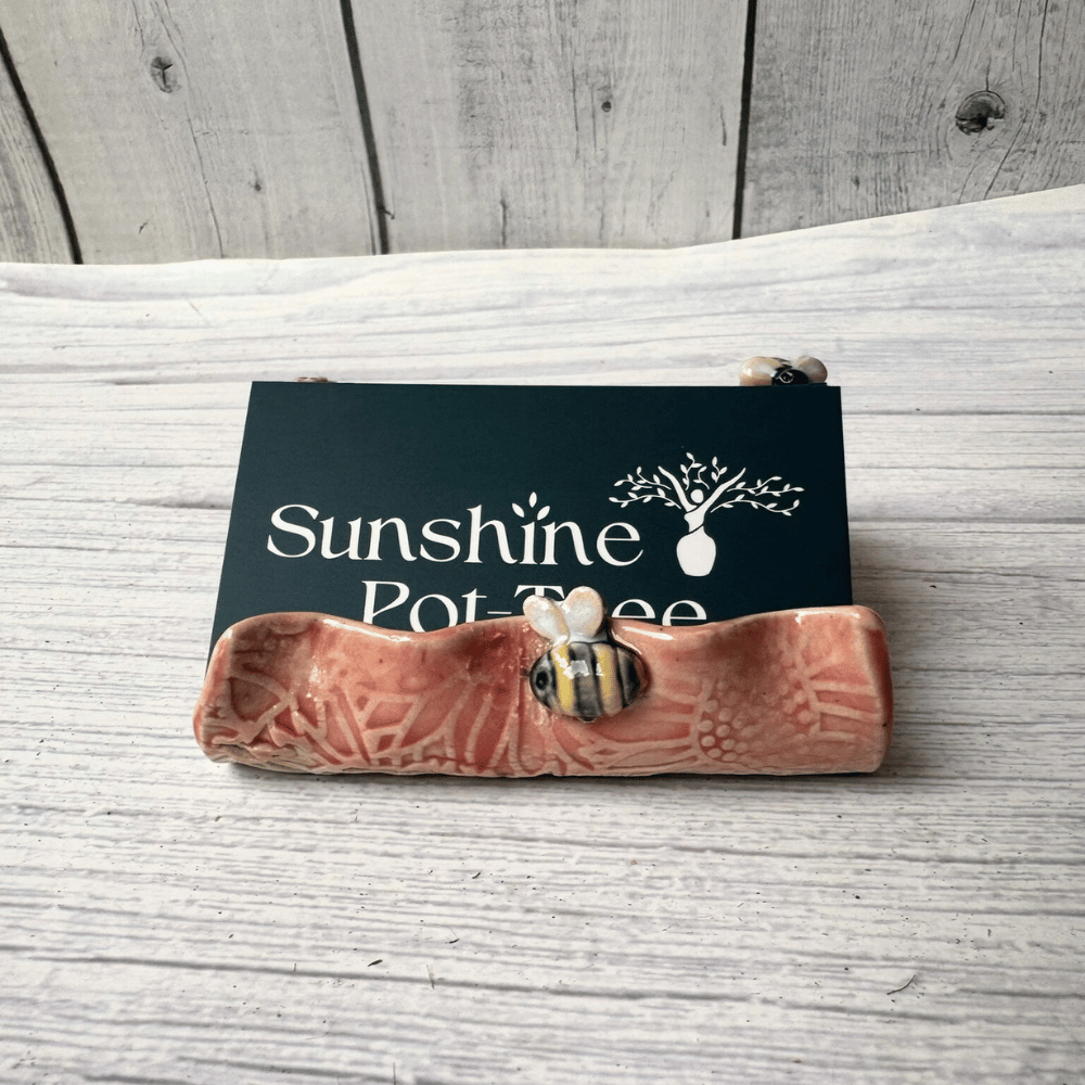Ceramic business card holder with floral and bee patterns on a wooden surface