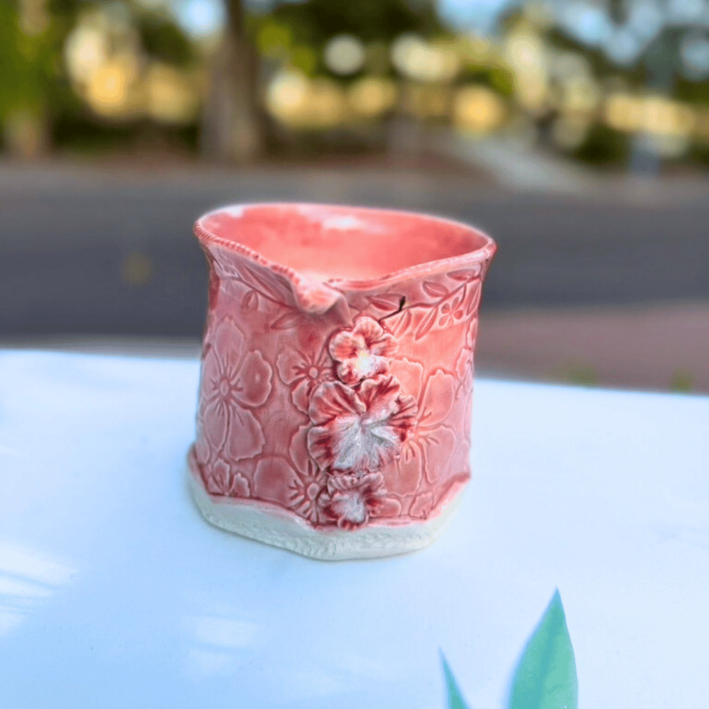 Pink ceramic planter with hibiscus floral patterns on a blurred natural background