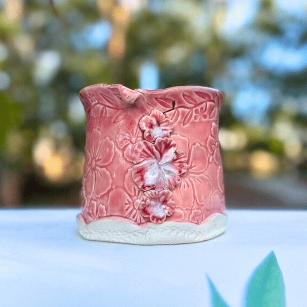 Pink ceramic planter with hibiscus floral patterns on a blurred natural background