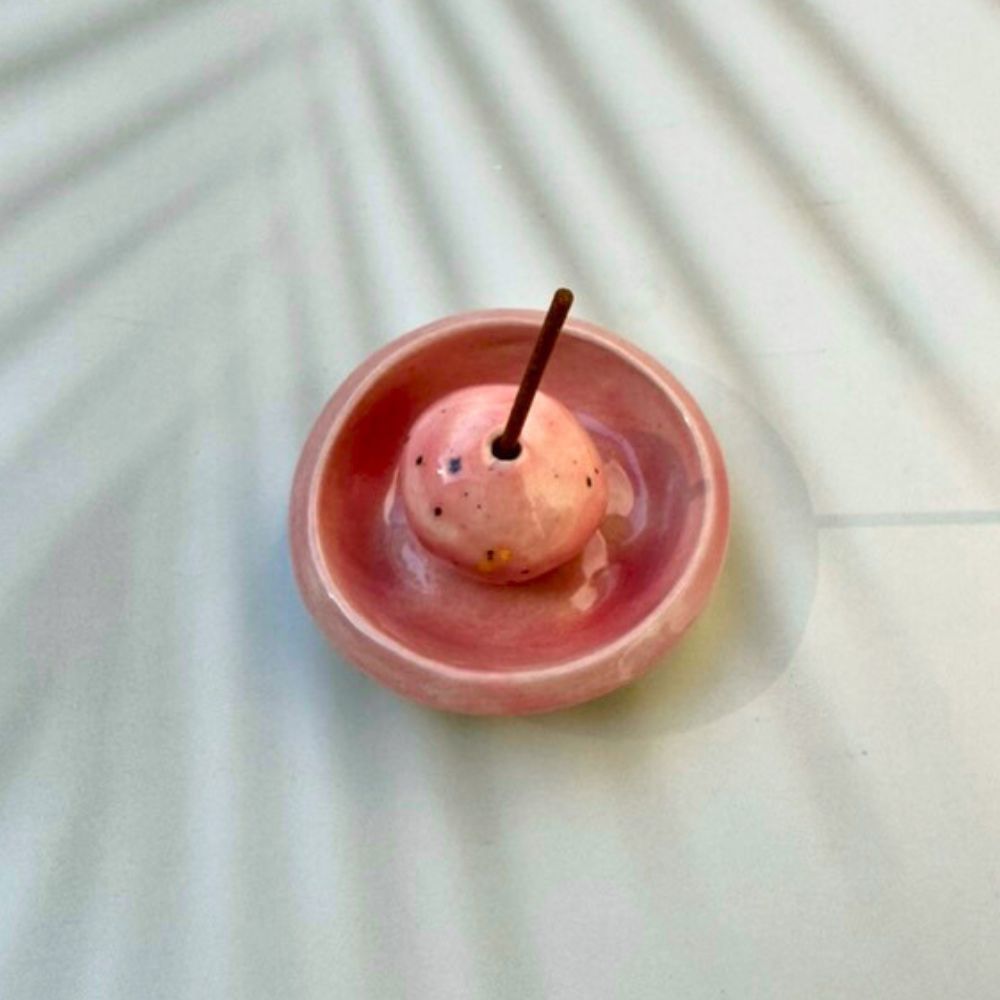 Pink ceramic incense holder with a small pink ball and incense stick on a light background
