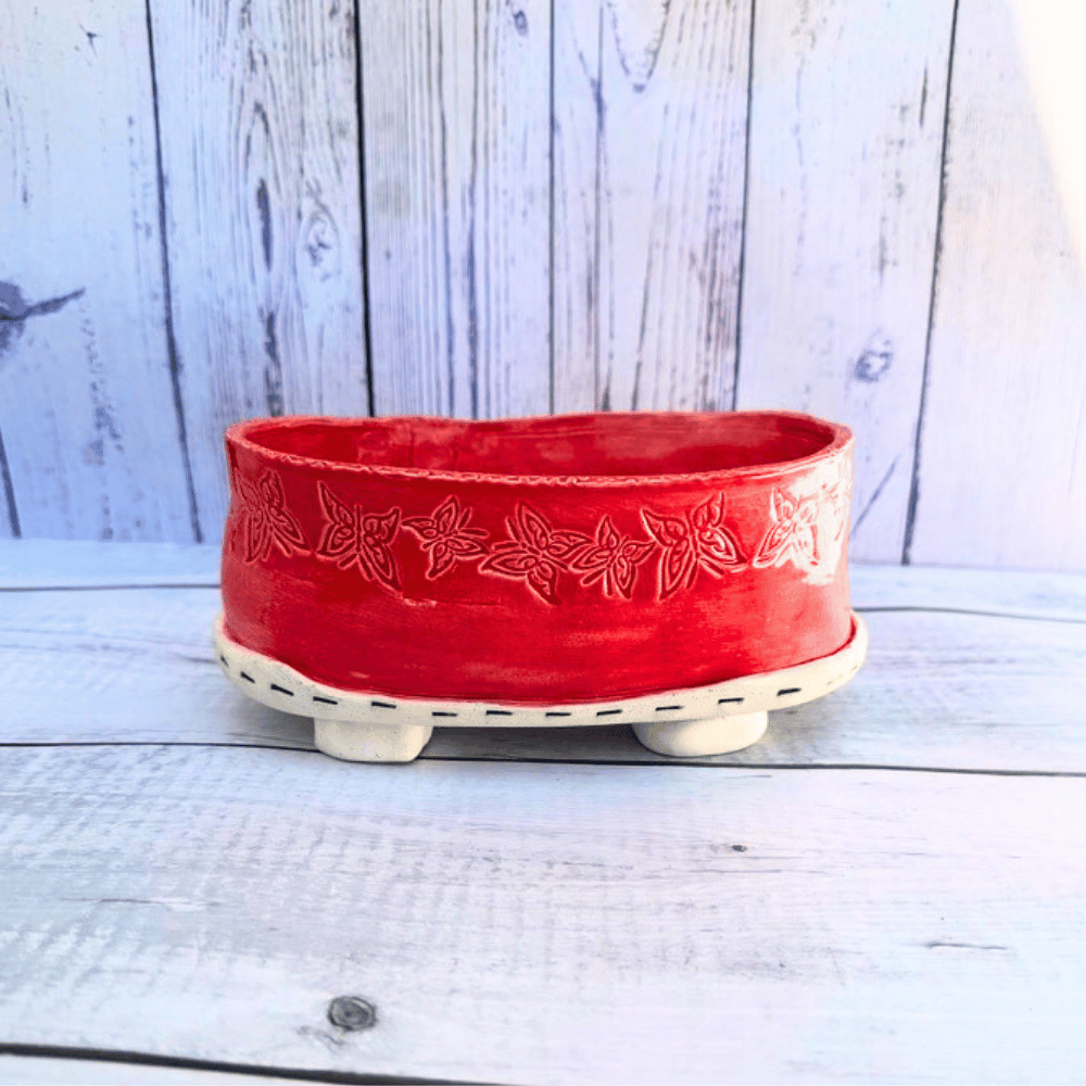 Red ceramic planter with butterfly patterns on a wooden surface