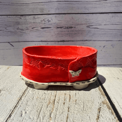Red ceramic planter with floral patterns on a wooden surface