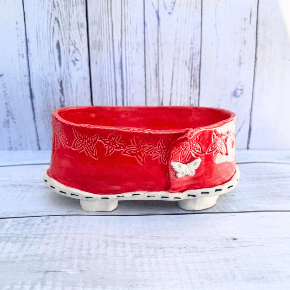 Red ceramic bonsai pot with butterfly design on a wooden surface