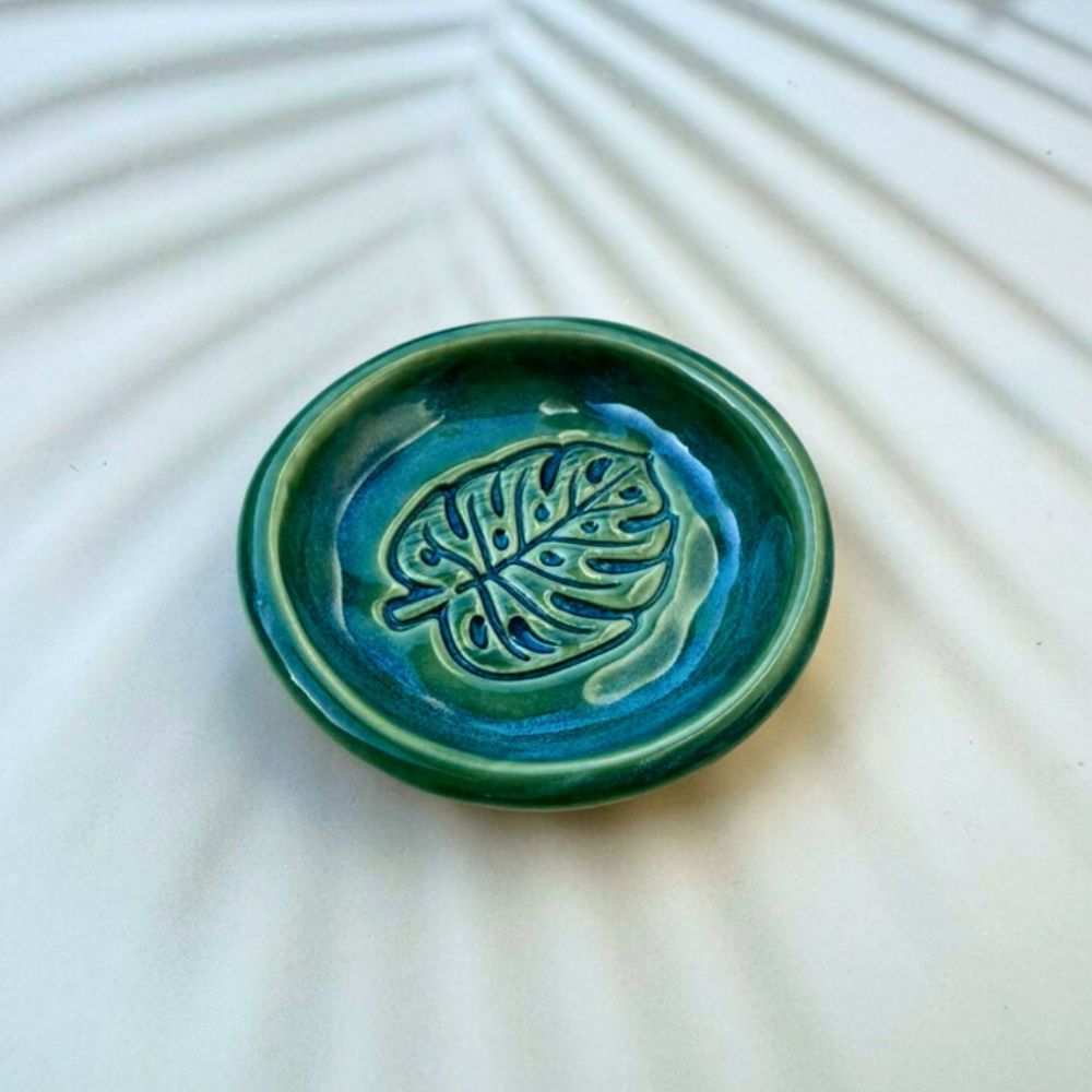 Green ceramic dish with leaf design on a textured white surface