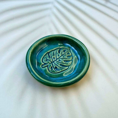 Green ceramic dish with leaf design on a textured white surface
