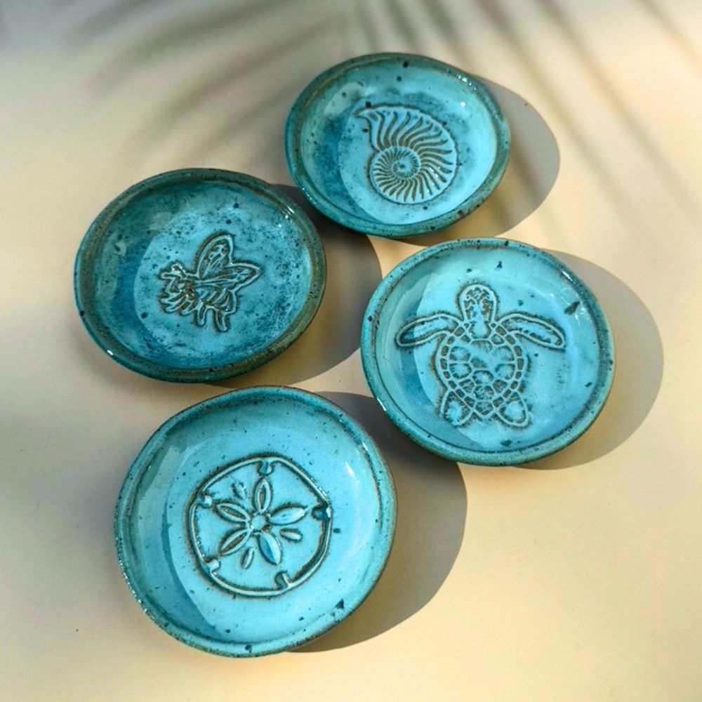 Four turquoise ceramic trinket dishes with embossed designs on a light background