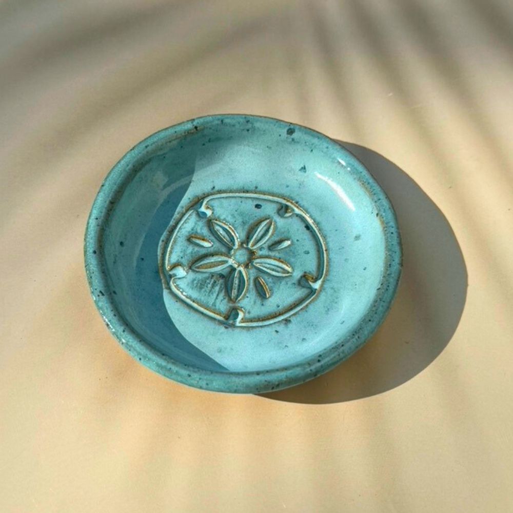 Turquoise ceramic dish with sand dolalr design on a beige surface
