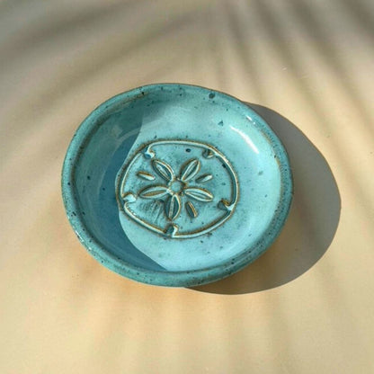 Turquoise ceramic dish with sand dolalr design on a beige surface