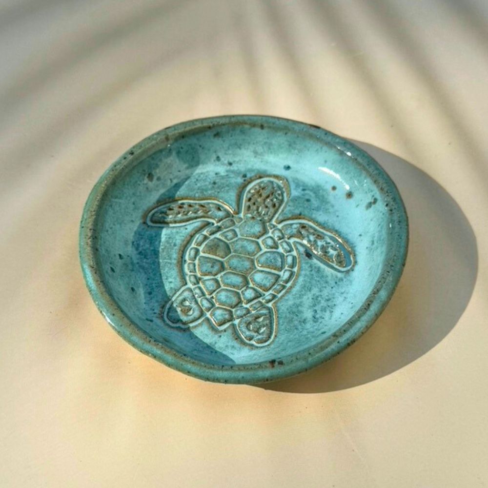 Turquoise ceramic dish with a turtle design on a beige background