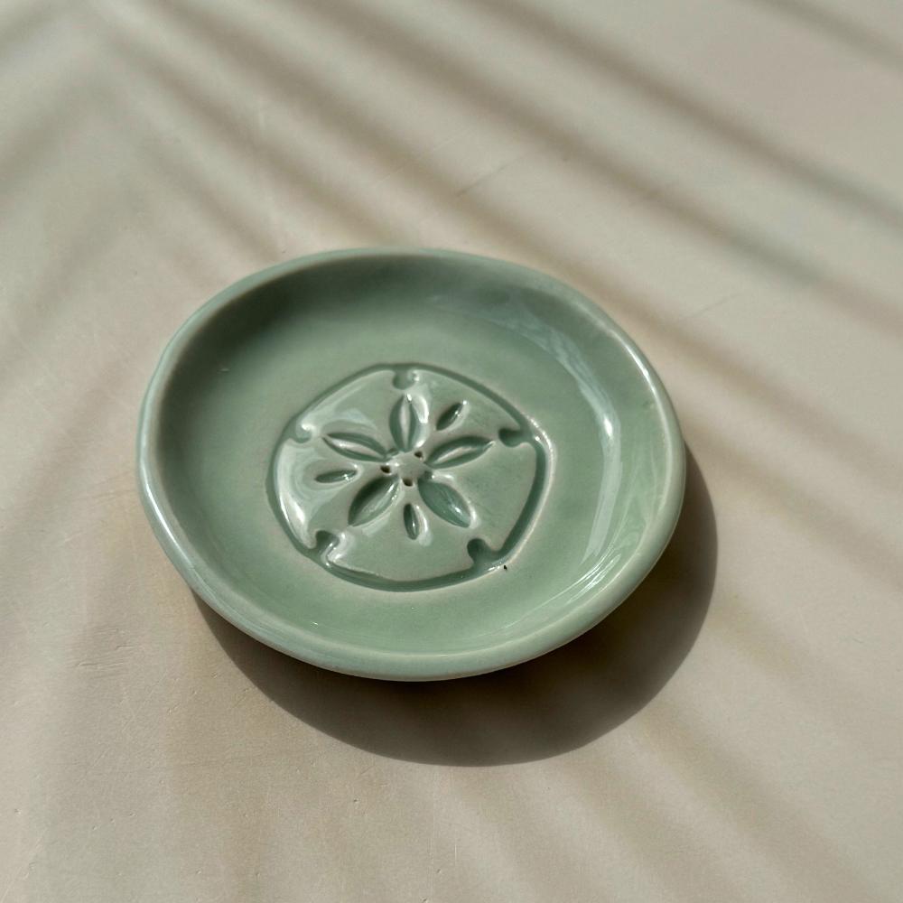 Green ceramic dish with sand dollar design on a beige surface