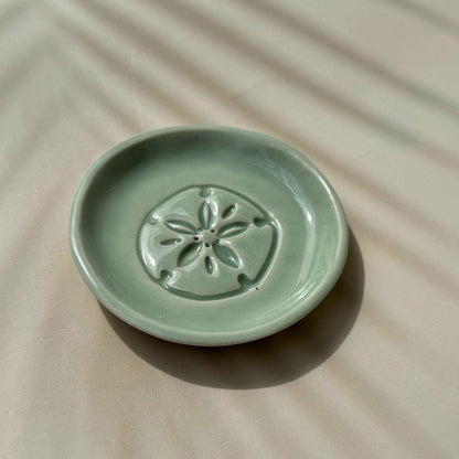 Green ceramic dish with sand dollar design on a beige surface