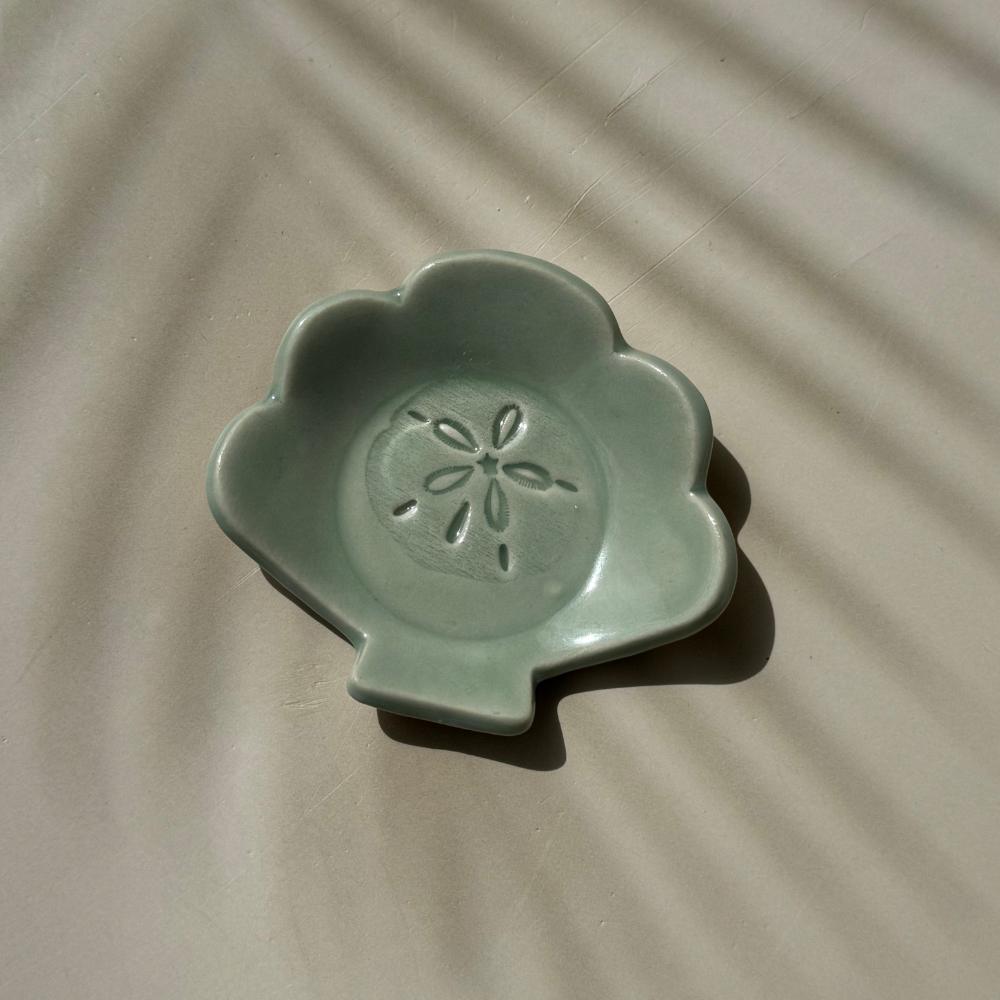 an aqua blue ceramic dish in the shape of a shell with sand dollar