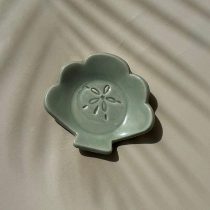 an aqua blue ceramic dish in the shape of a shell with sand dollar