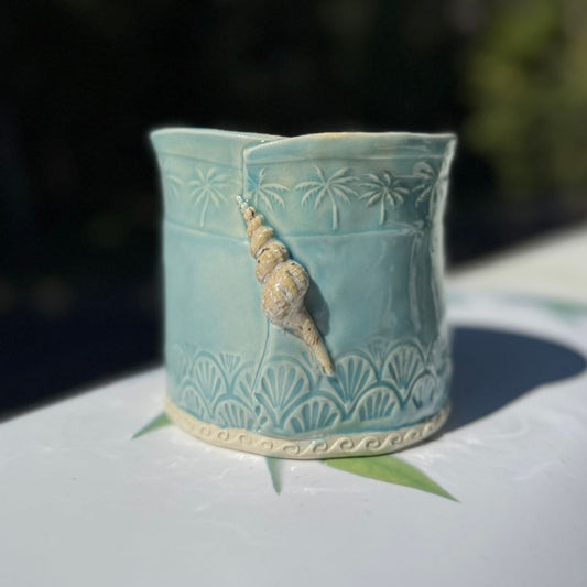 Teal ceramic planter with shell decoration on a white surface
