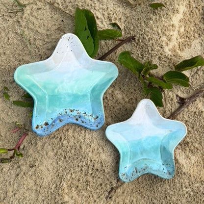 Two star-shaped blue ceramic dishes on sandy ground with green leaves.