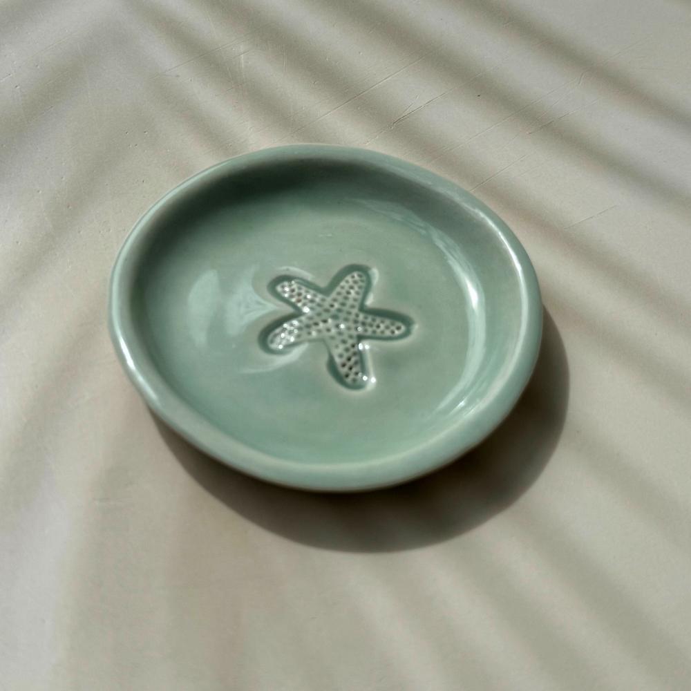 Green ceramic dish with a starfish design on a beige surface