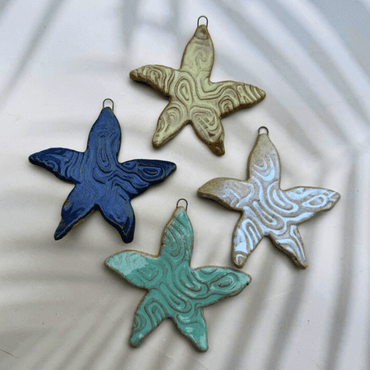 Four ceramic starfish ornaments in blue, green, and brown on a textured white background