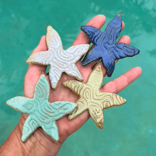 Hand holding four starfish shaped ceramic ornaments against a teal background