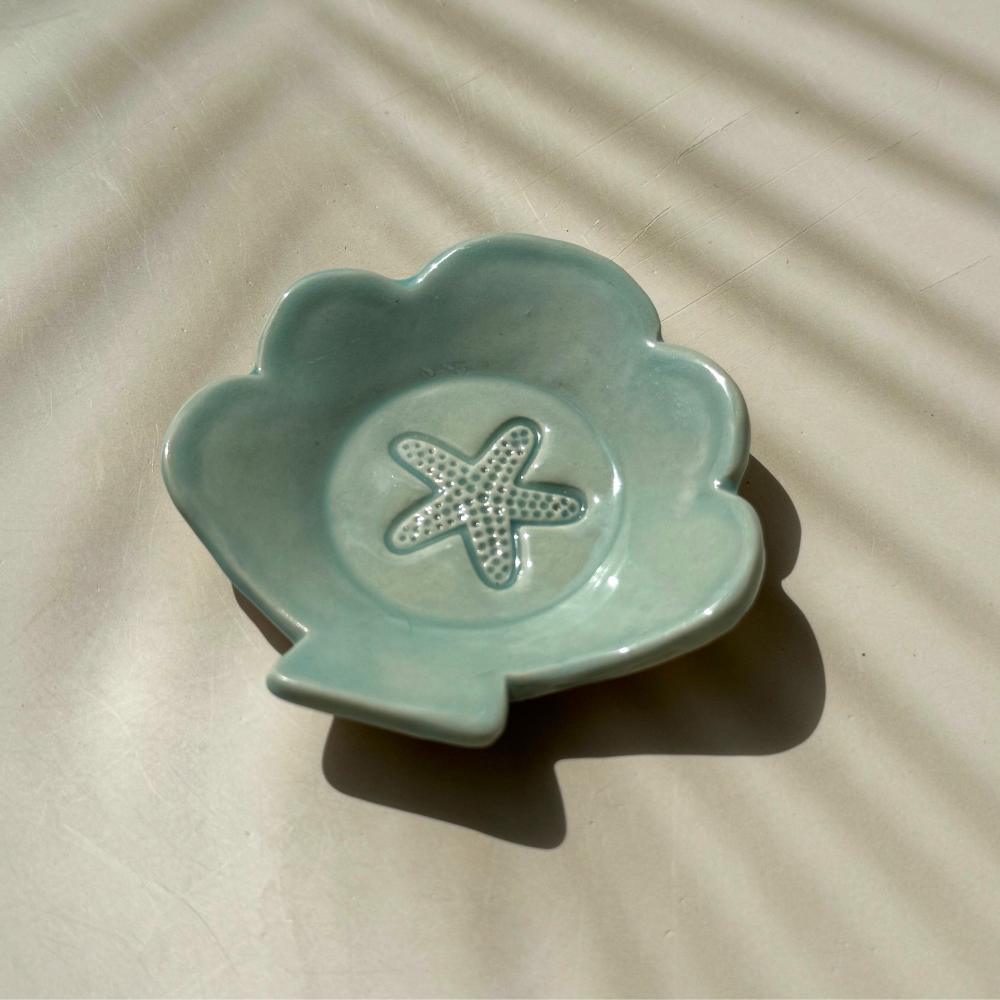 an aqua blue ceramic dish in the shape of a shell with starfish