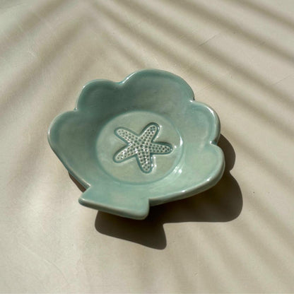 an aqua blue ceramic dish in the shape of a shell with starfish