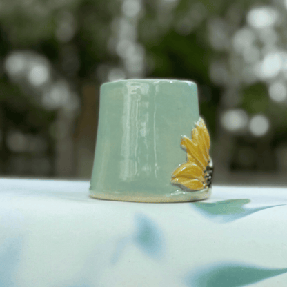 Green ceramic cup with a sunflower design on a blurred natural background