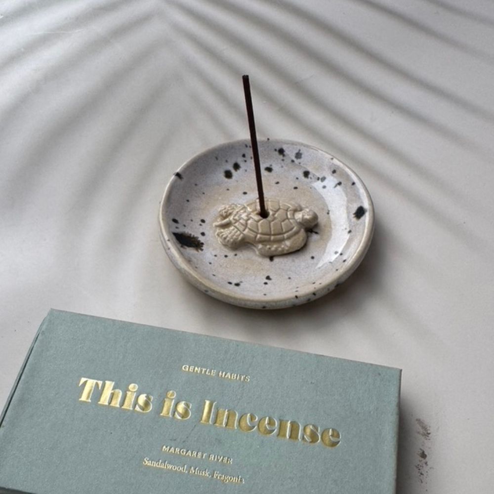 Incense stick in a ceramic holder with a book titled 'This is Incense' on a textured surface