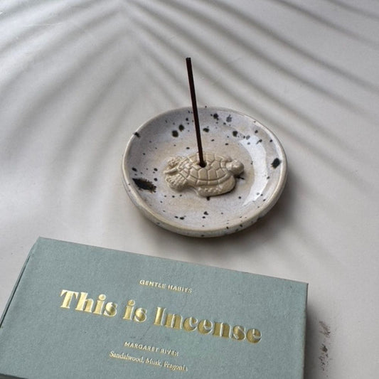 Incense stick in a ceramic holder with a book titled 'This is Incense' on a textured surface