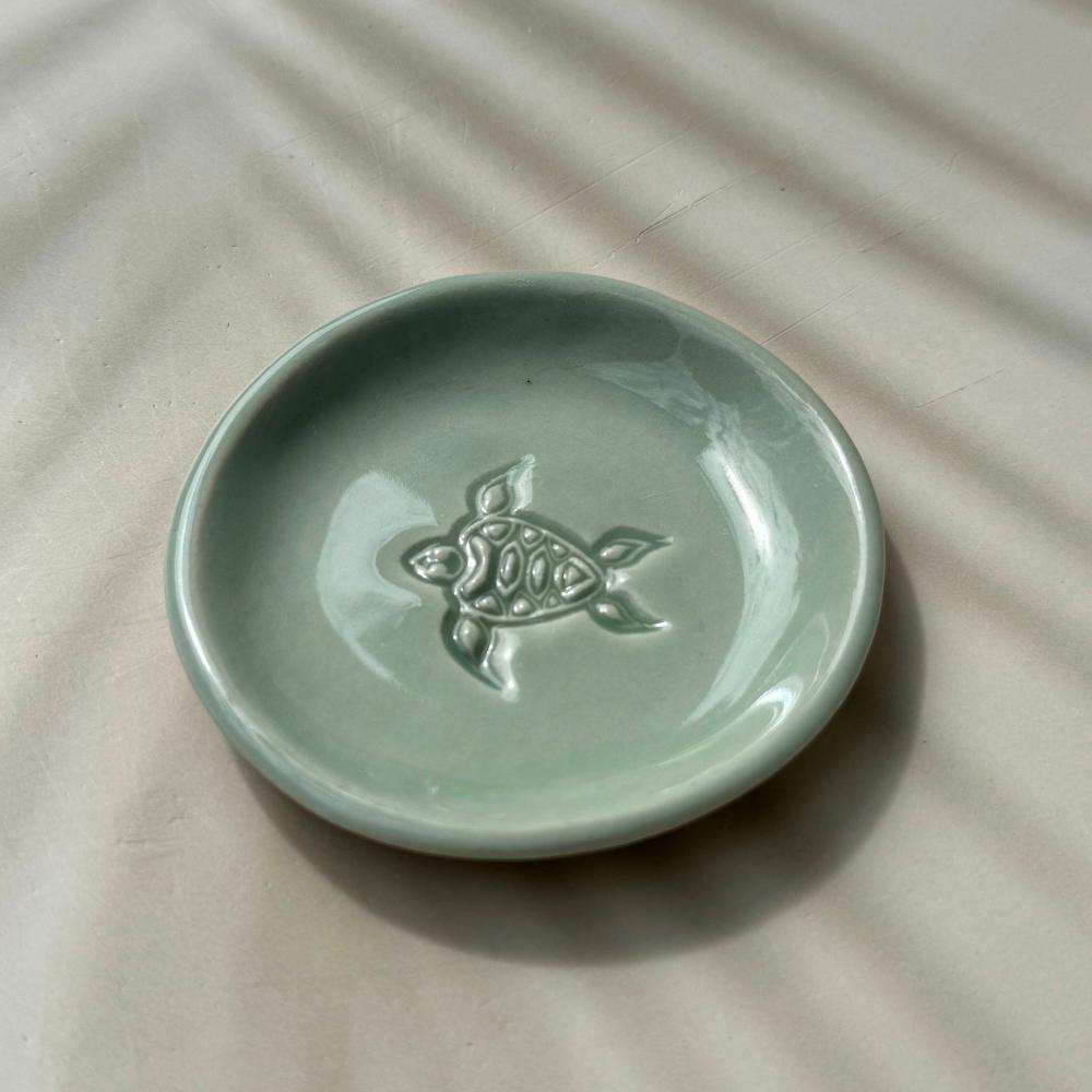 Green ceramic dish with a turtle design on a beige surface