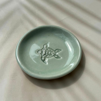 Green ceramic dish with a turtle design on a beige surface