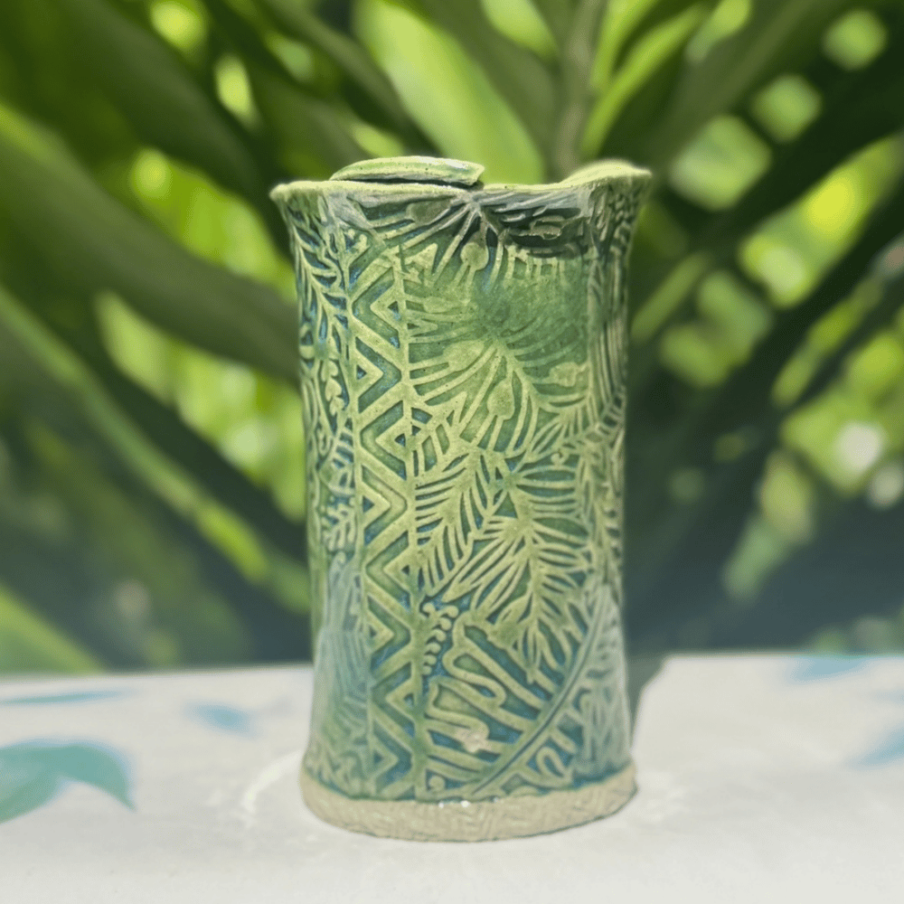 Green ceramic vase with leaf pattern on a white surface with a blurred green background